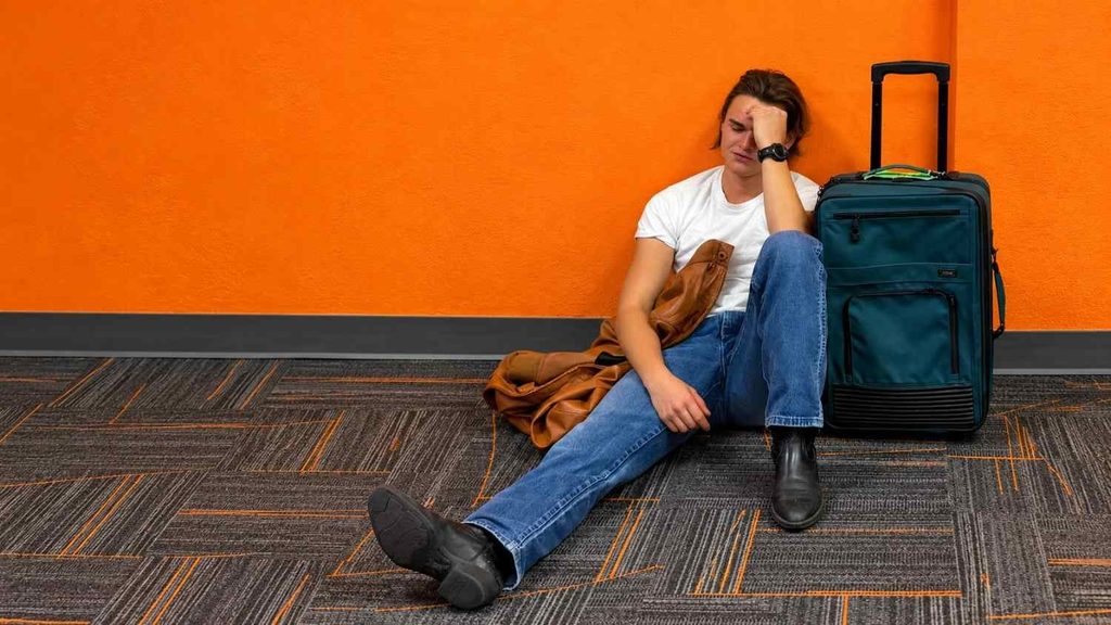 Tired traveler resting with luggage at an airport after a long flight
